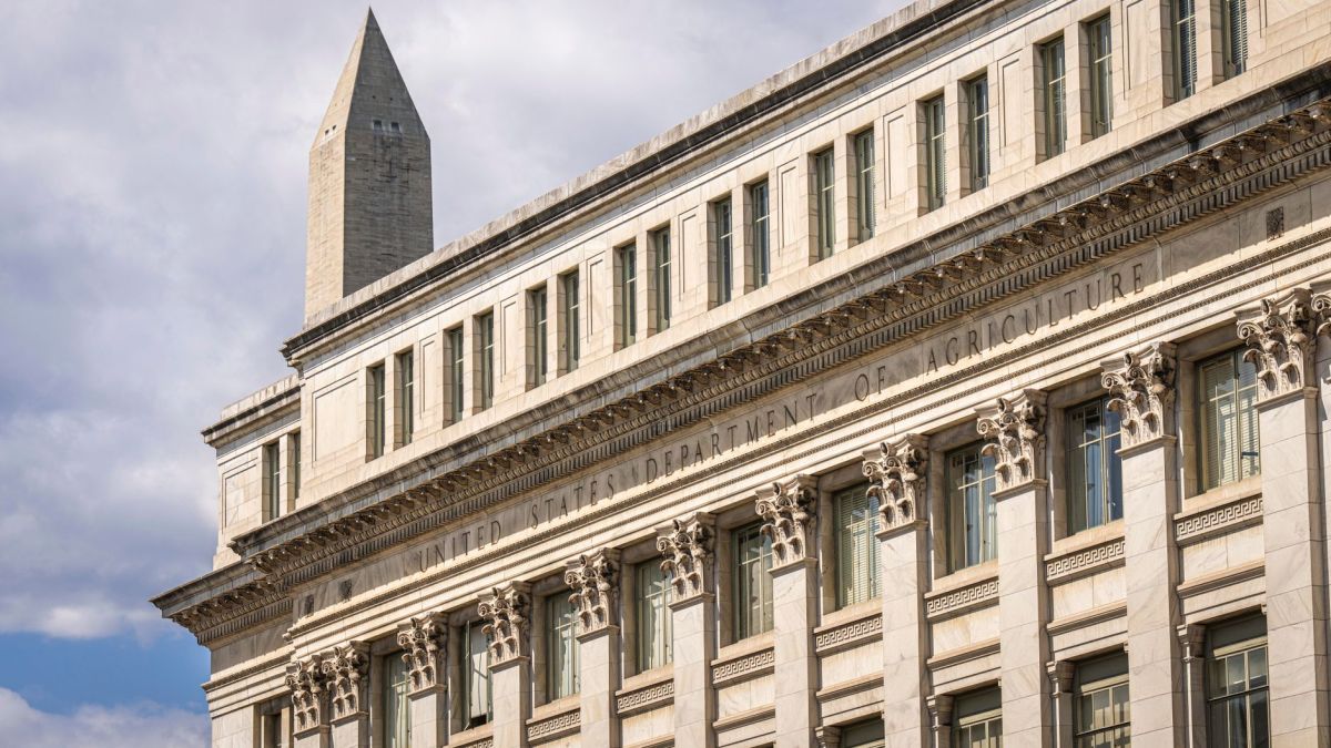 US Department of Agriculture building with Washington Monument behind, blue sky with clouds.