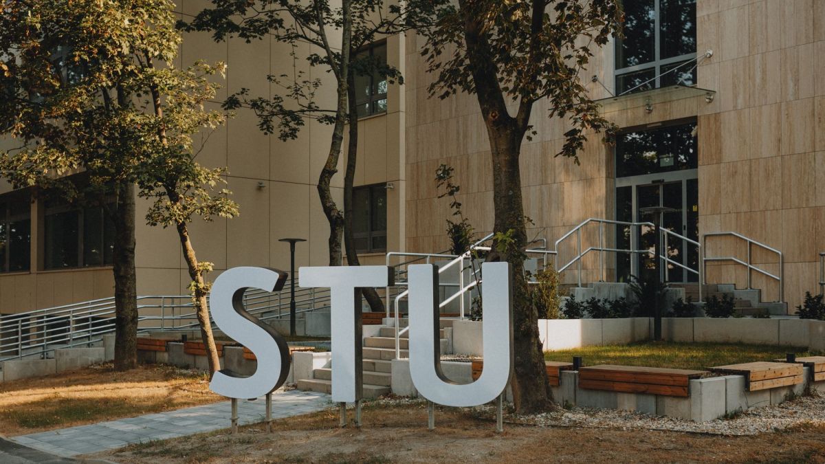 Modern building entrance with large STU letters surrounded by greenery and urban design.