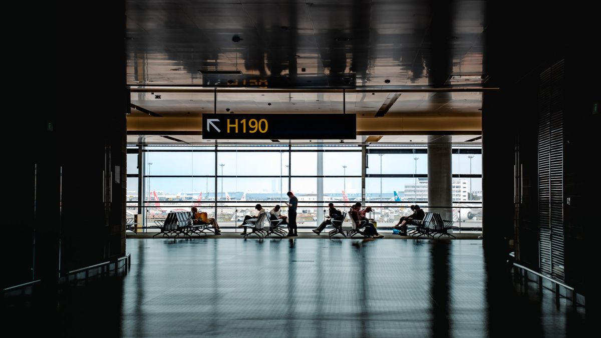 Silhouetted travelers waiting at Shanghai airport terminal gate H190 with cityscape view.
