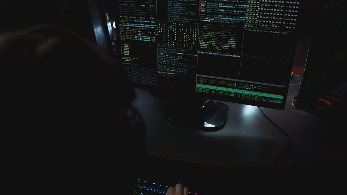 Dark room setup with code displayed on PC monitors highlighting cybersecurity themes.