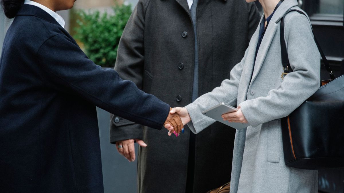 Crop anonymous diverse businesswomen in trendy elegant coats shaking hands after important conference on street