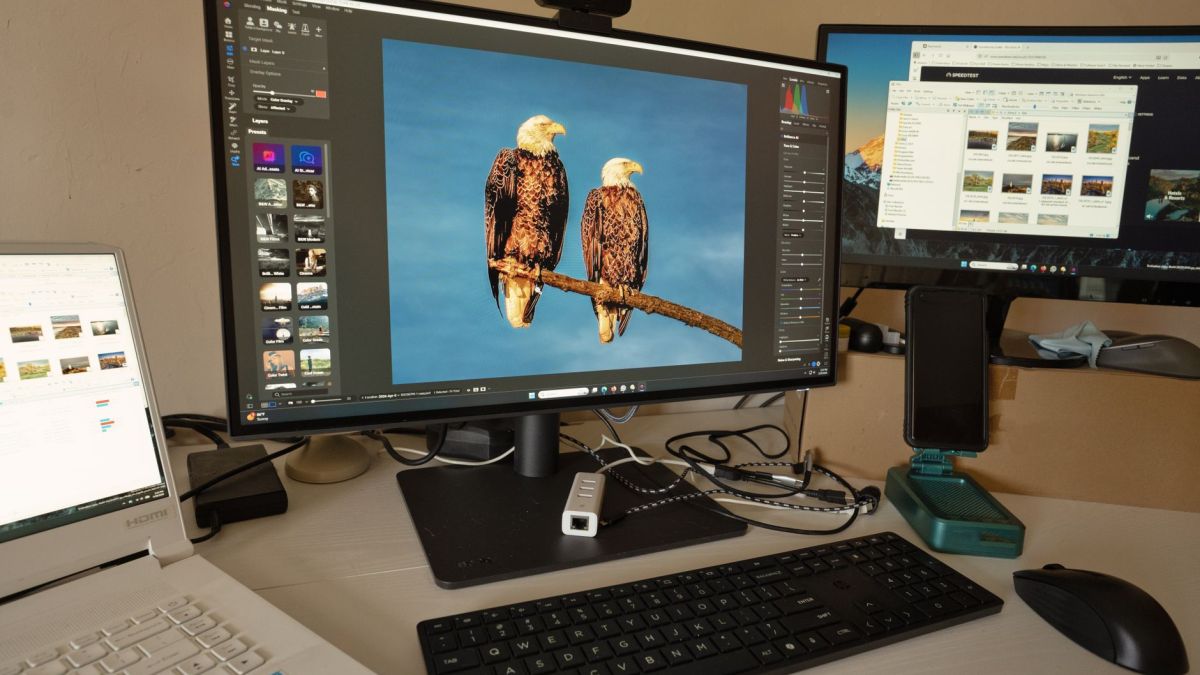 A desk setup showing photo editing software on multiple monitors, a keyboard, and peripherals.