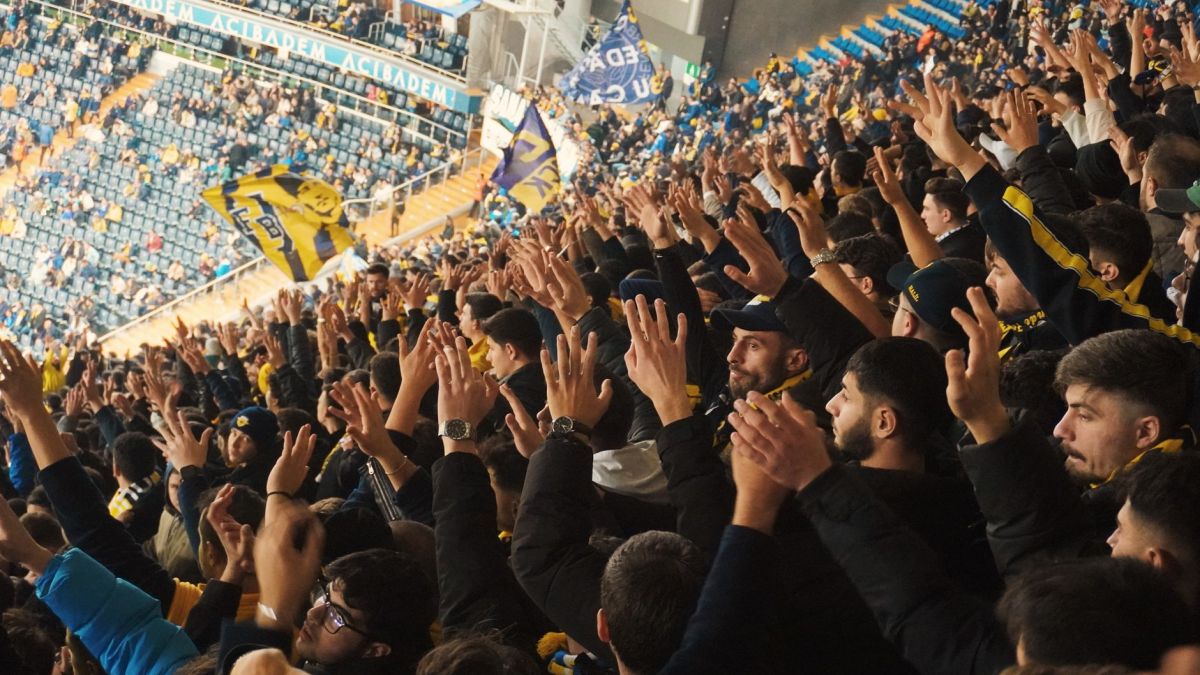 Energetic fans with raised hands in a stadium, supporting their soccer team with enthusiasm.
