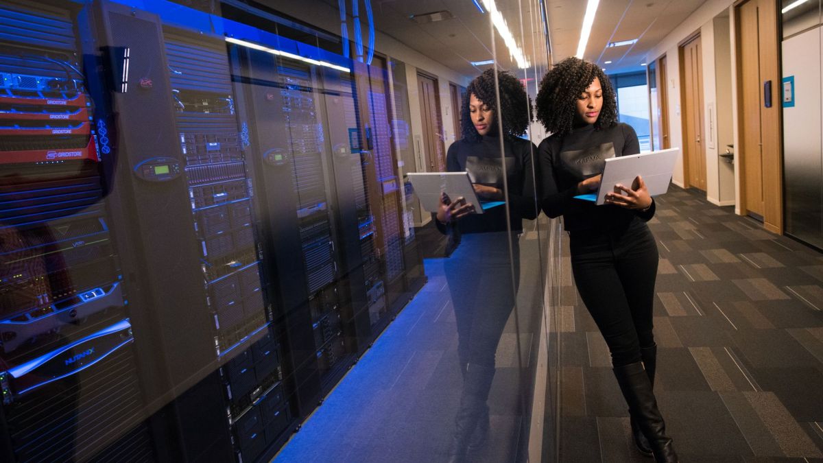 A woman using a laptop navigating a contemporary data center with mirrored servers.