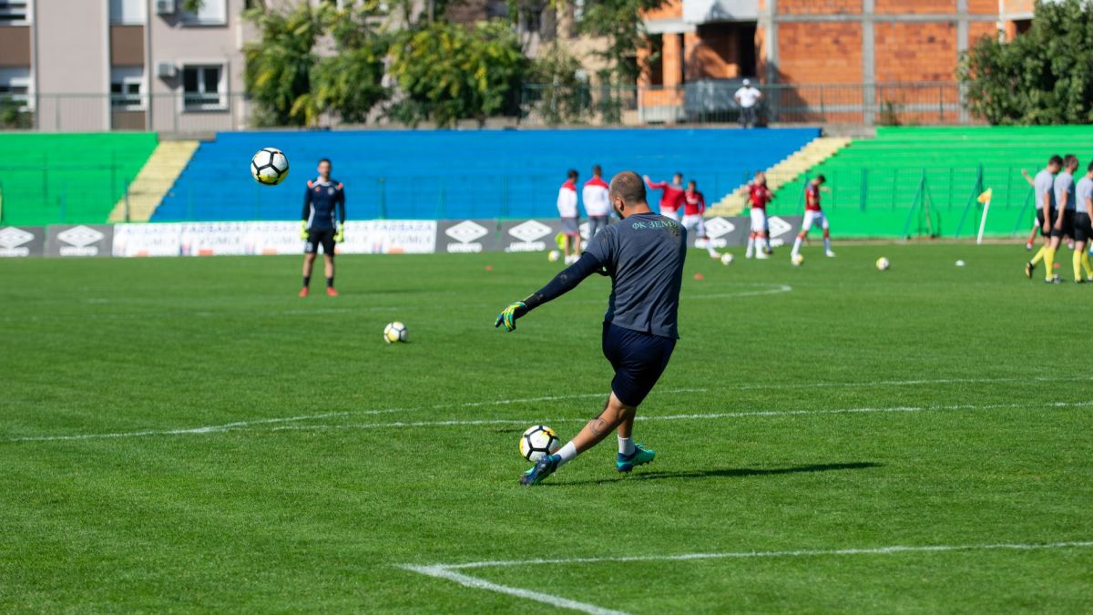 Soccer player kicking a ball during training on a green field under sunny skies.