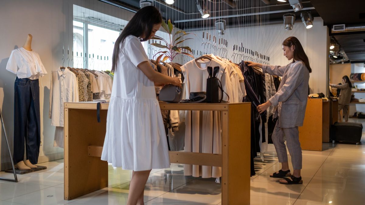Two women browsing clothes in a modern indoor fashion store.
