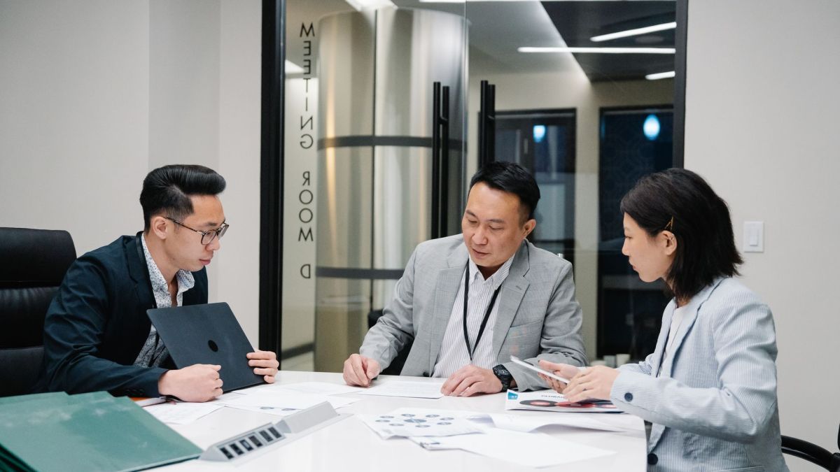 Business meeting with three professionals collaborating in a modern conference room setting.