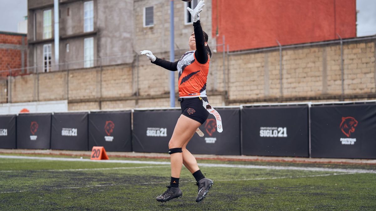 A female athlete jumps to catch a football during a game on an outdoor sports field.