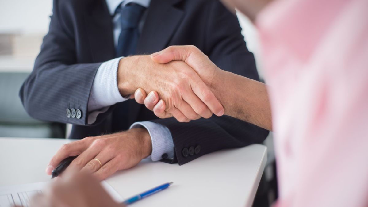 Two businessmen shaking hands across table, symbolizing agreement and partnership in an office environment.
