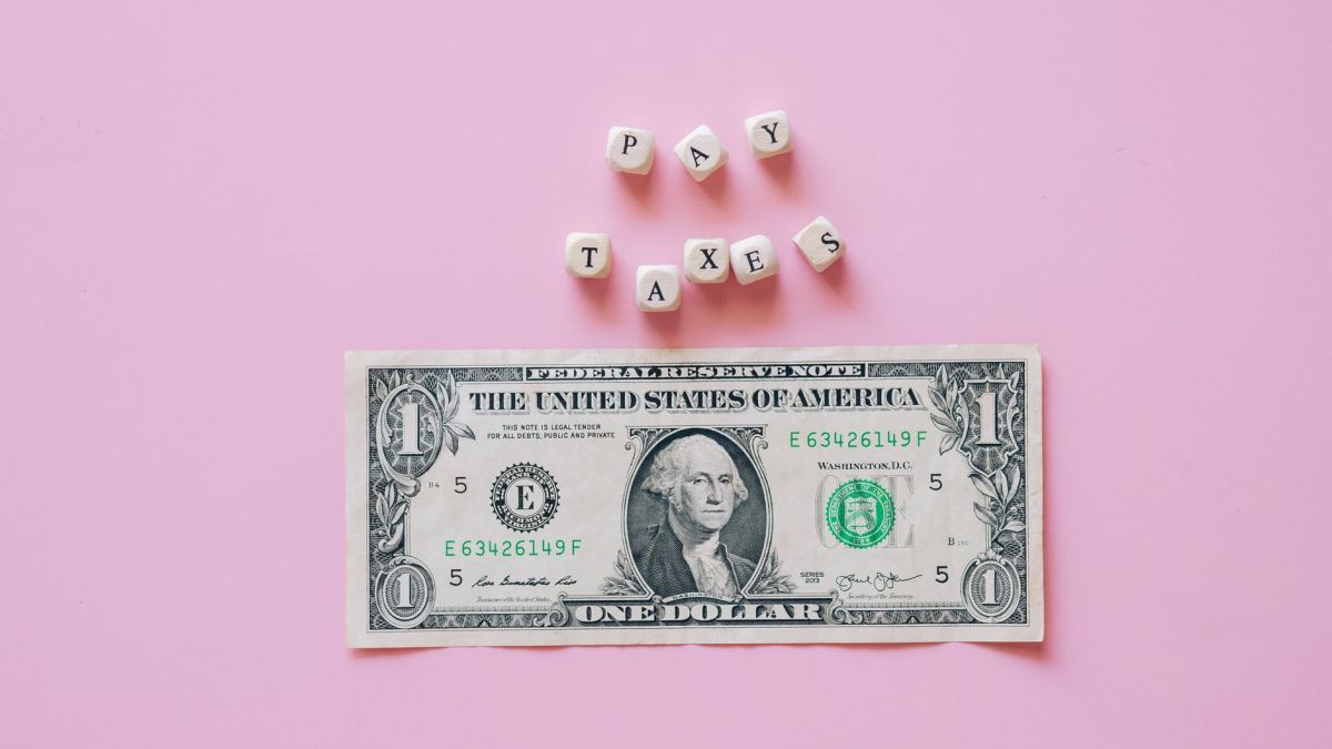 US one dollar bill on a pink background with pay taxes reminder cubes.