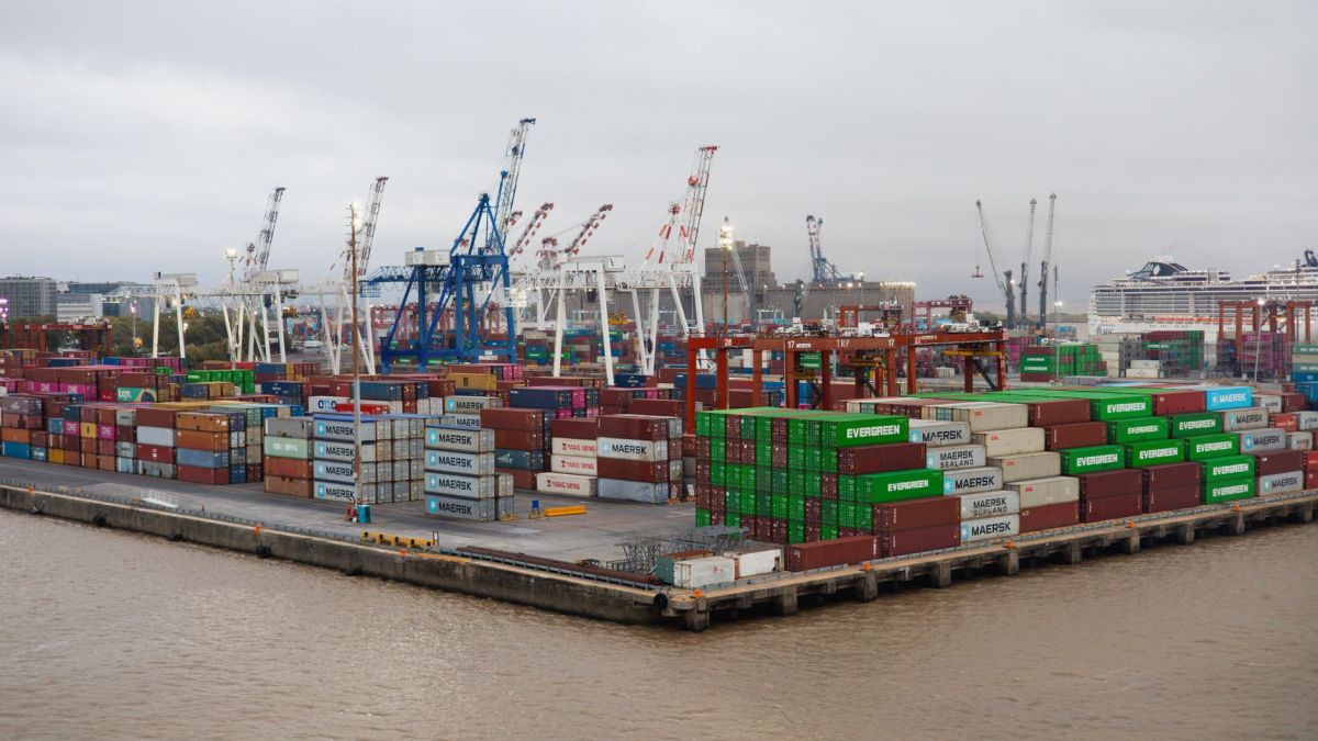 A bustling shipping port with stacked cargo containers and cranes under overcast skies.