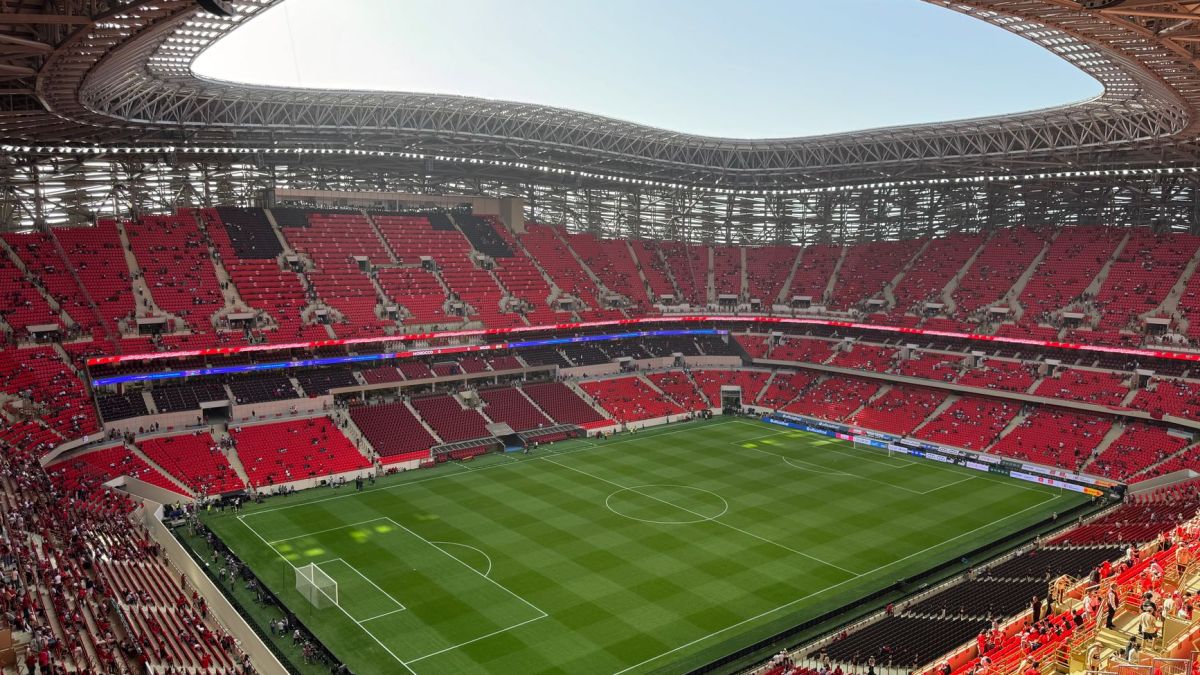 Aerial view of a modern stadium with vibrant red seats and a well-maintained green field.