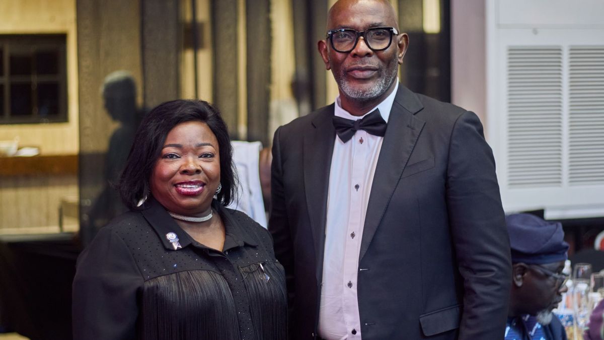 Two elegantly dressed individuals at a black tie event indoors, smiling for the camera.