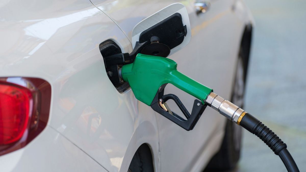 Close-up of a green nozzle refueling a white car at a gas station.
