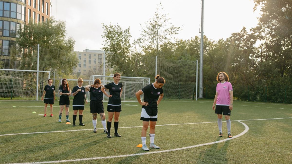 Women's soccer team practices drills on a sunny outdoor field with coach observing.
