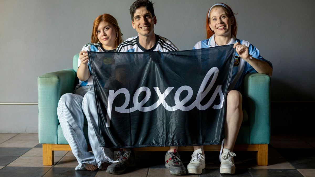Group of three people holding an Argentina-themed flag indoors, showcasing team spirit.