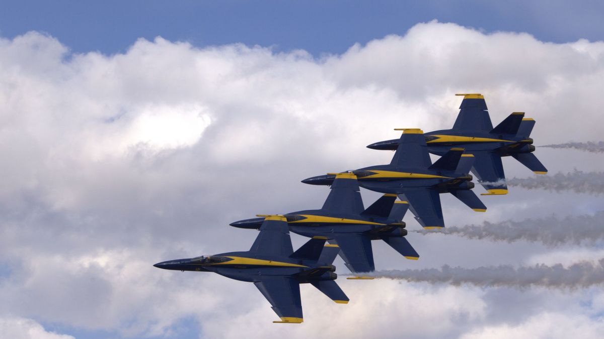 Four military jets performing an aerial formation against a blue sky with clouds.
