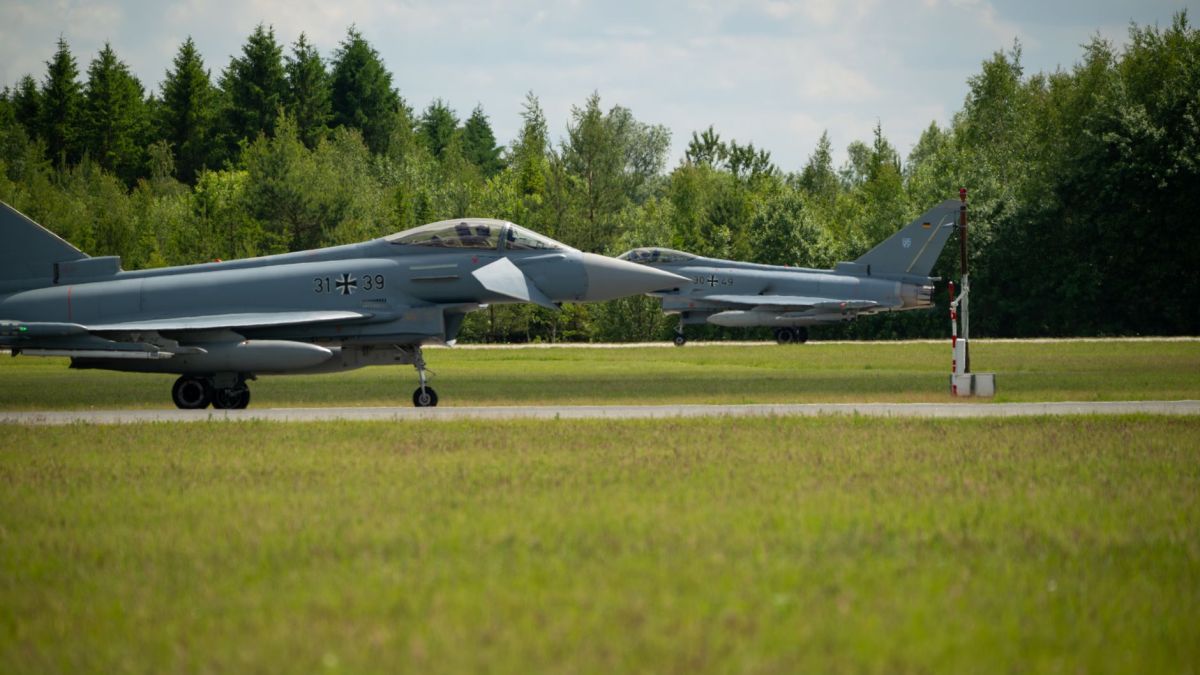 Two German fighter jets aligned on a runway surrounded by lush greenery.