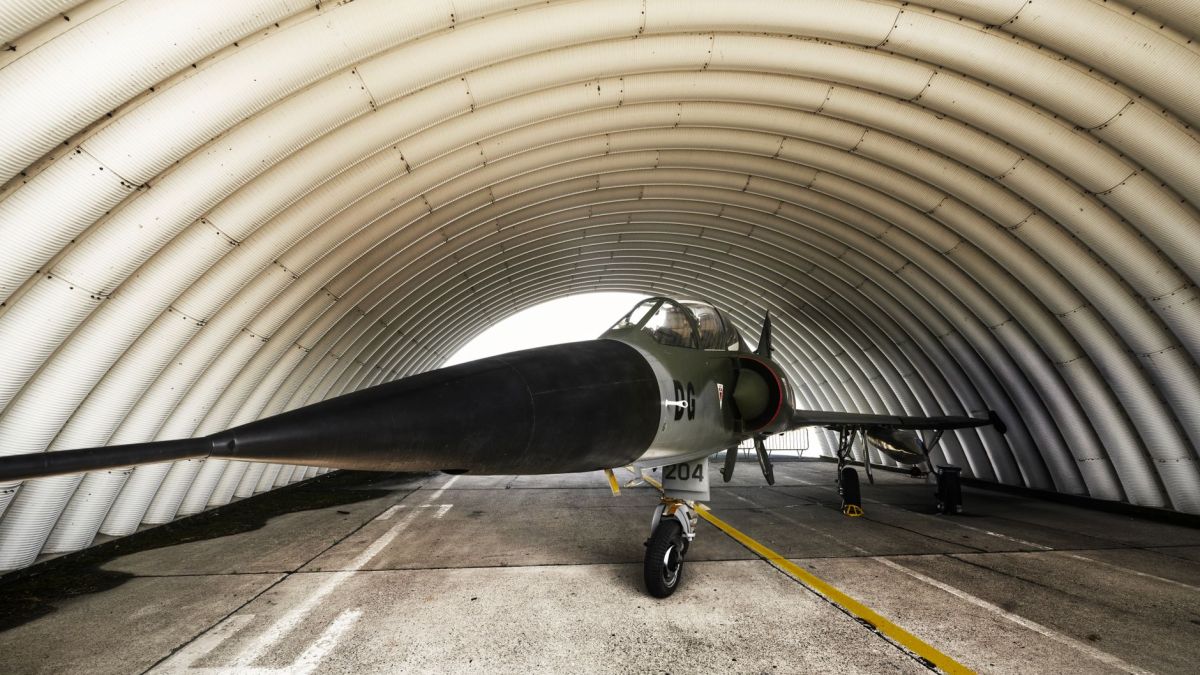 A fighter jet parked inside an arched military hangar, showcasing its sleek design.