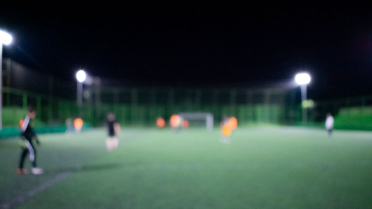 Blurred image of a nighttime football match under bright stadium lights with players on the field.