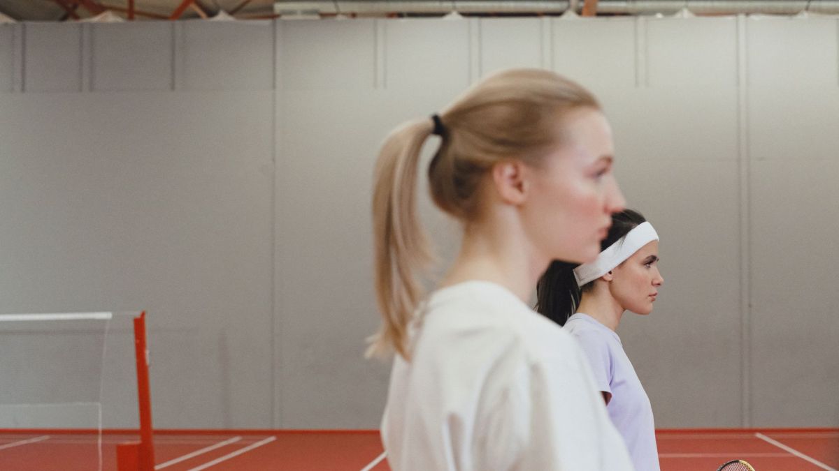 Two women playing tennis indoors with focus on their profiles. Ready for the game.