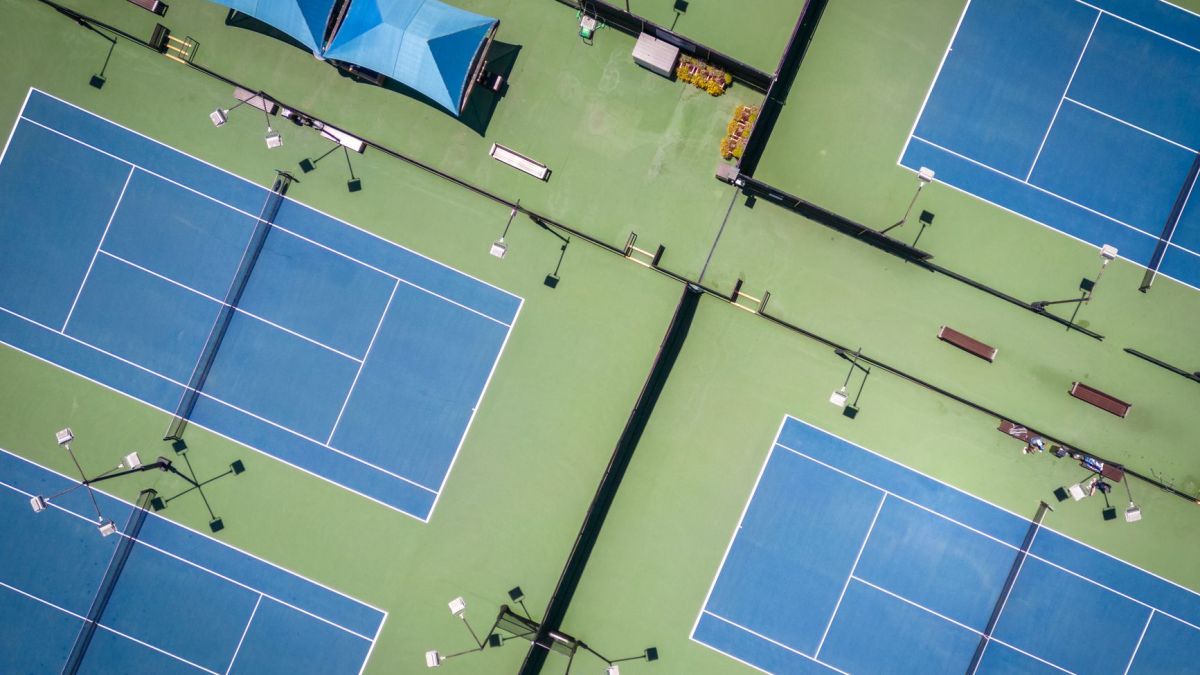 Aerial view of multiple blue tennis courts with striking geometric patterns.