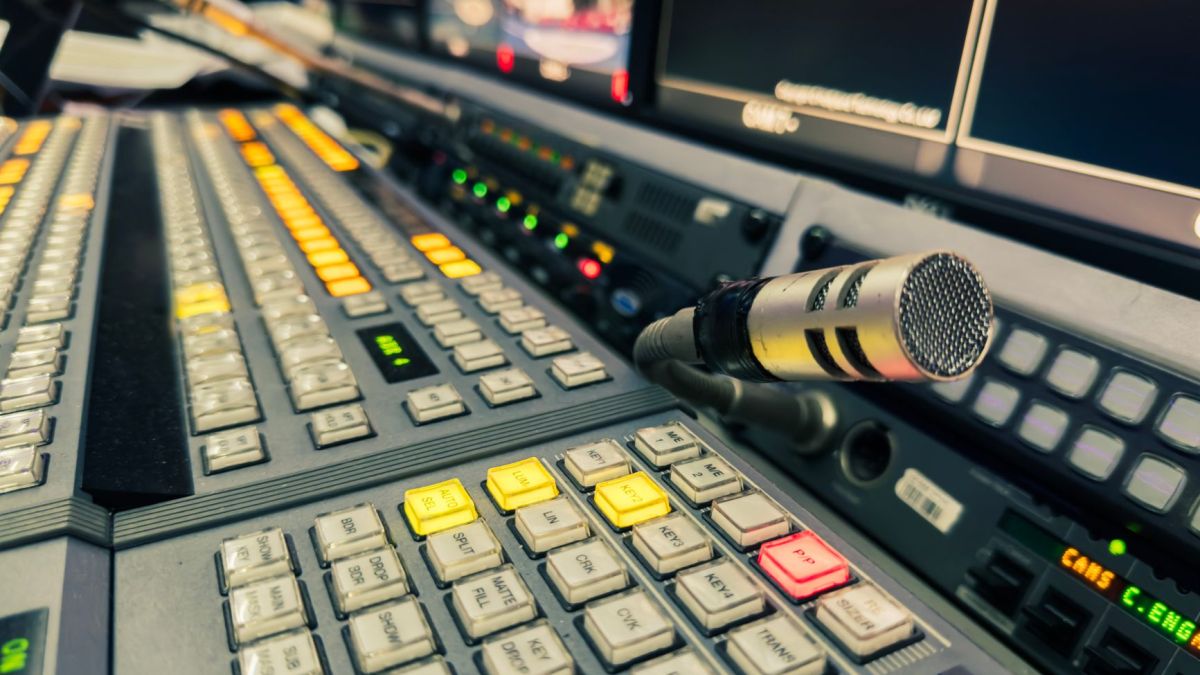 Detailed view of a broadcasting studio control panel with a microphone and multiple screens.