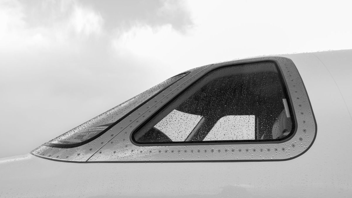 Close-up of rain-speckled airplane window in grayscale, showcasing aviation detail.