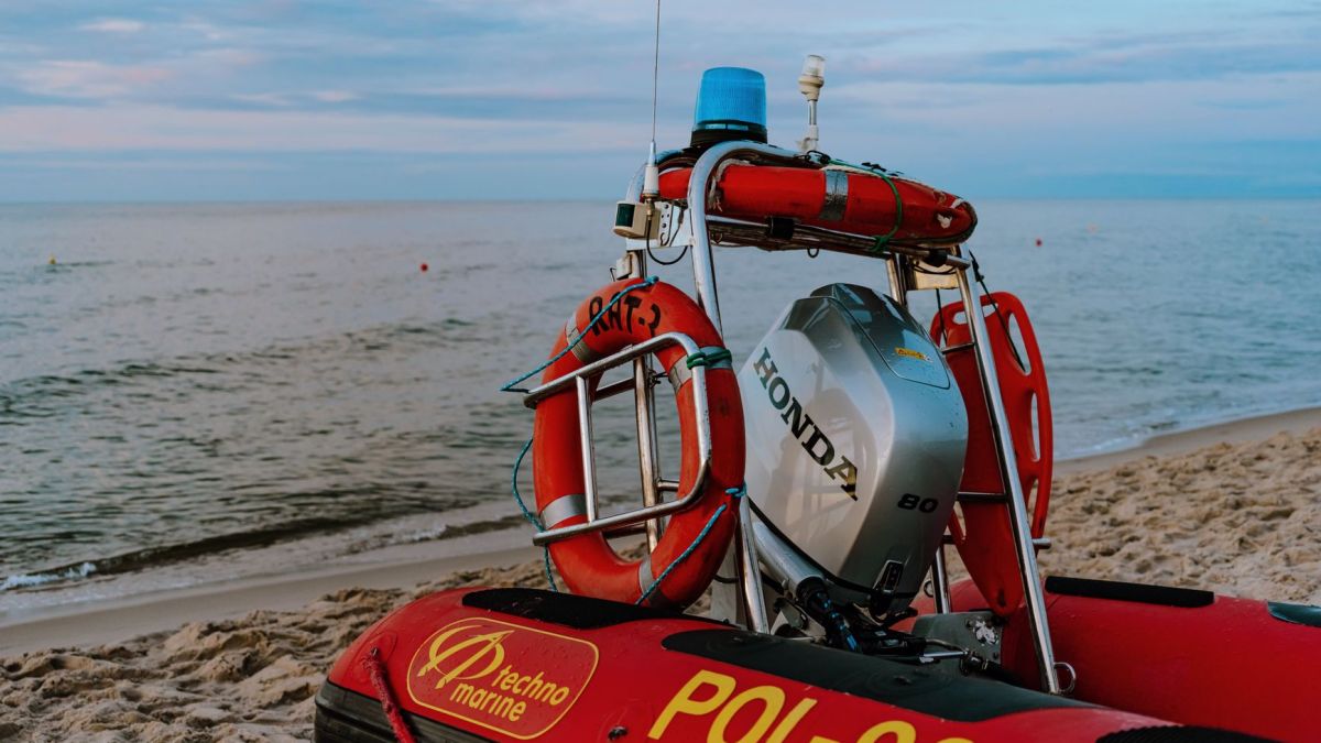 A red inflatable motorboat equipped with a Honda engine on a sandy beach at dawn.
