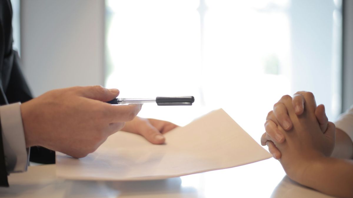 Side view of faceless formal man giving pen and paper to focused female with clenched hands at table on meeting