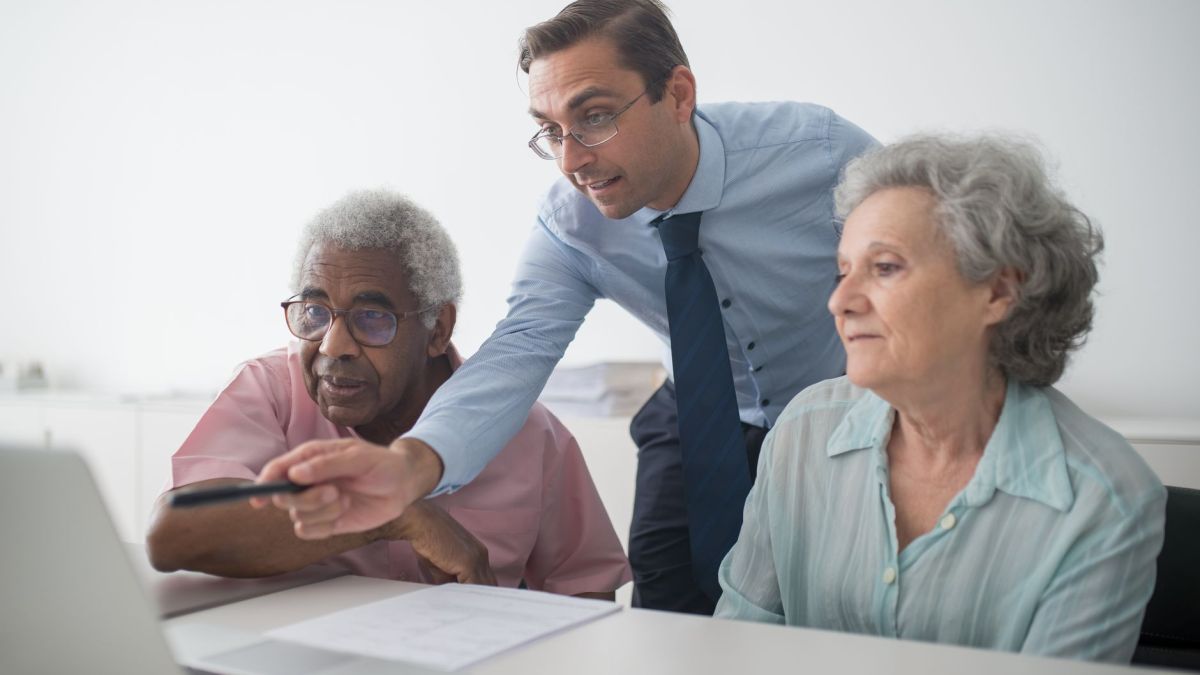 A business consultant explaining financial options to senior clients, using a laptop for illustration.