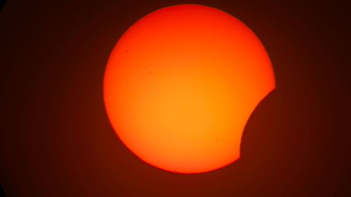 Dramatic close-up of a partial solar eclipse against a dark sky, vivid orange hues.
