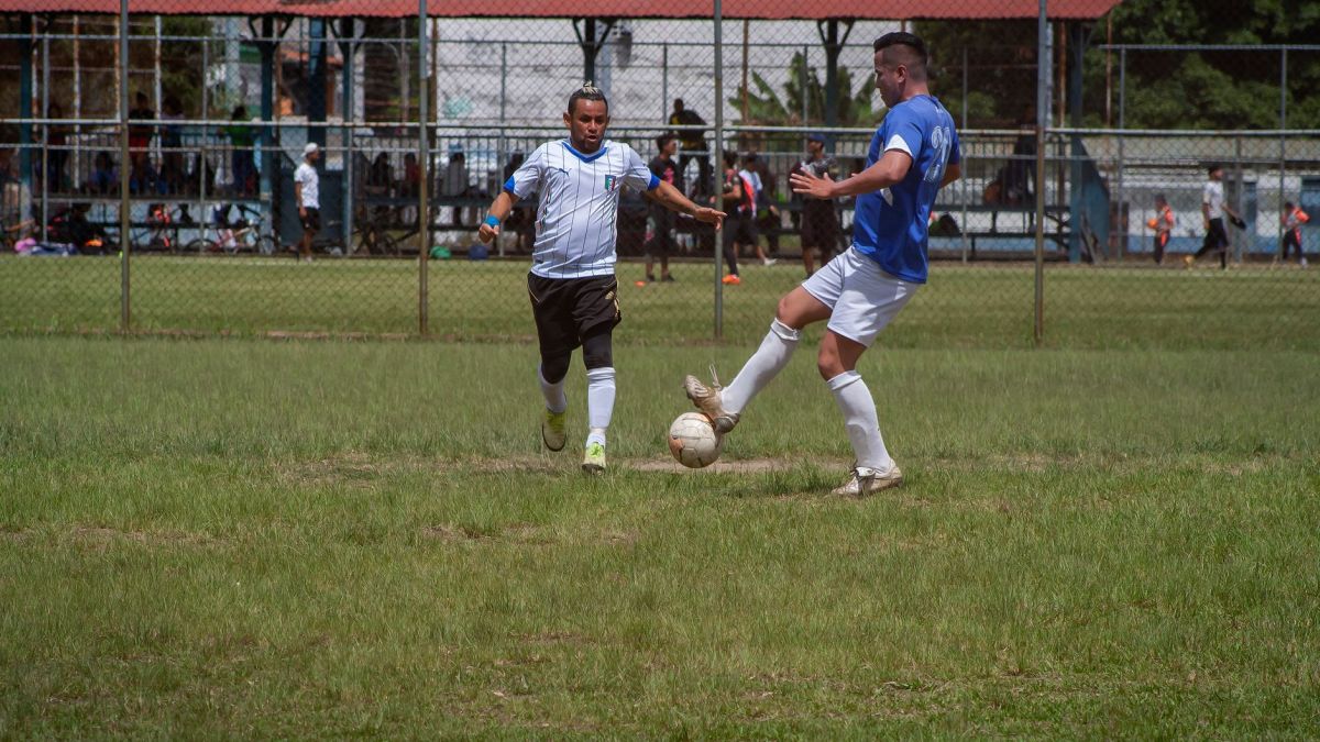 Two male soccer players competing in an outdoor match on a sunny day.