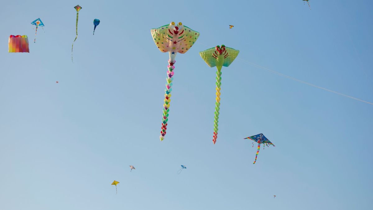 Brightly colored kites of various shapes fly high against a clear blue sky in Ho Chi Minh City, Vietnam.