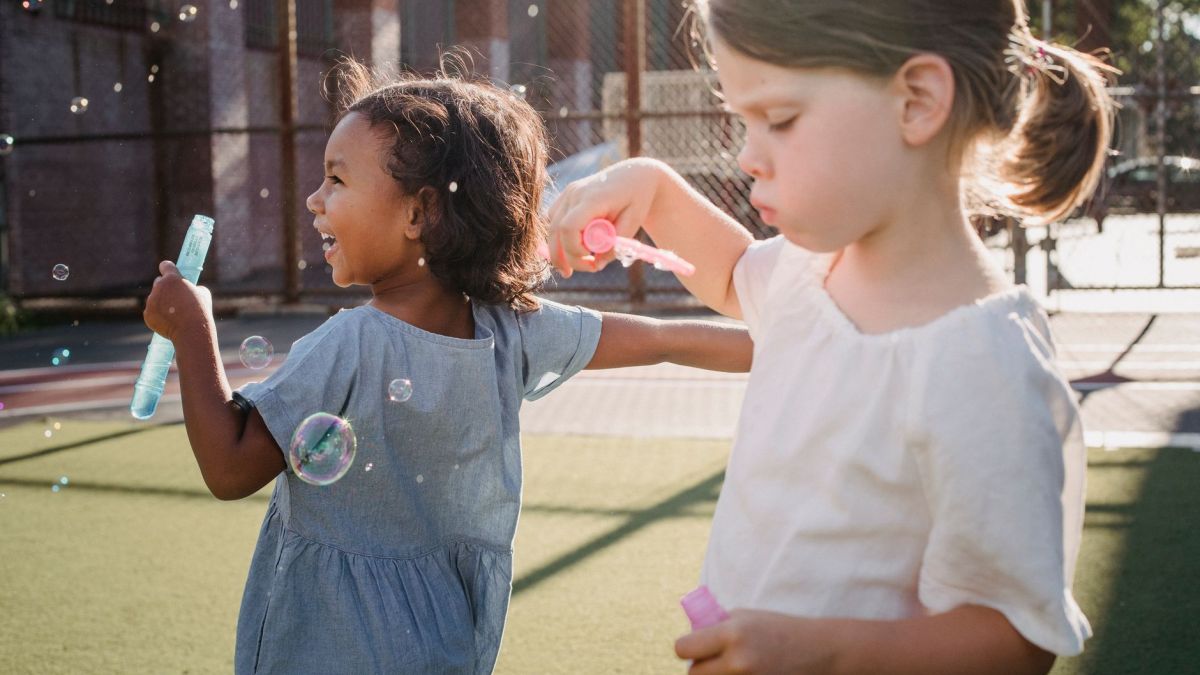 Two young girls enjoy playing with soap bubbles in a sunny outdoor setting, capturing joy and leisure.
