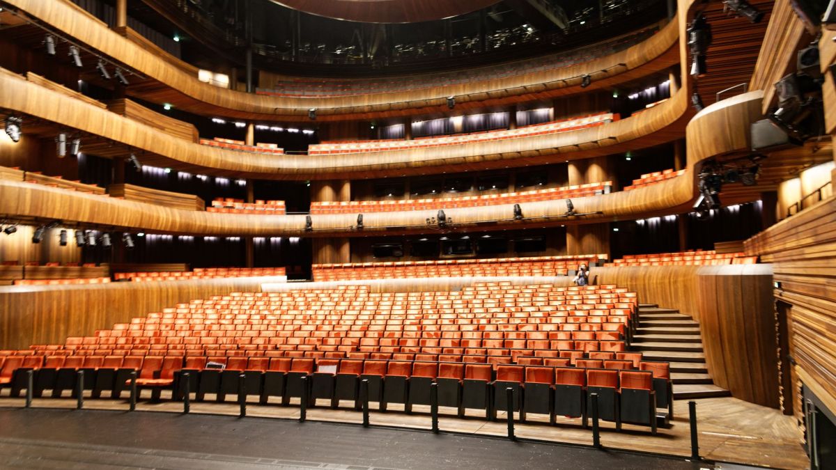 A spacious and modern indoor theatre featuring wooden interior and illuminated seating.