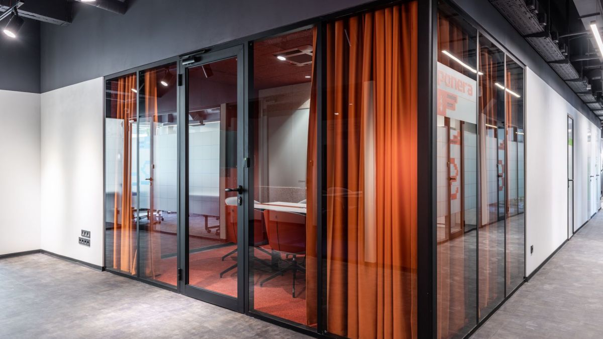 Hall of spacious contemporary business center with glass walls of modern office with colorful armchairs at table and red curtain
