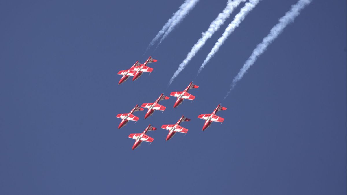 Seven red jets perform a precise aerial formation against a clear blue sky.