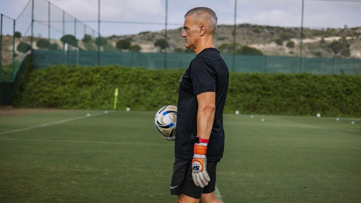 Experienced coach holding a soccer ball during football practice outdoors.