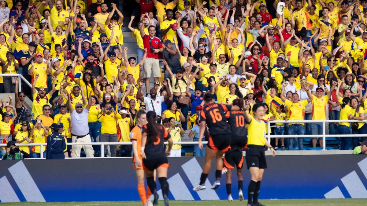 Energetic crowd of Colombian football fans cheering at a match in a vibrant stadium.