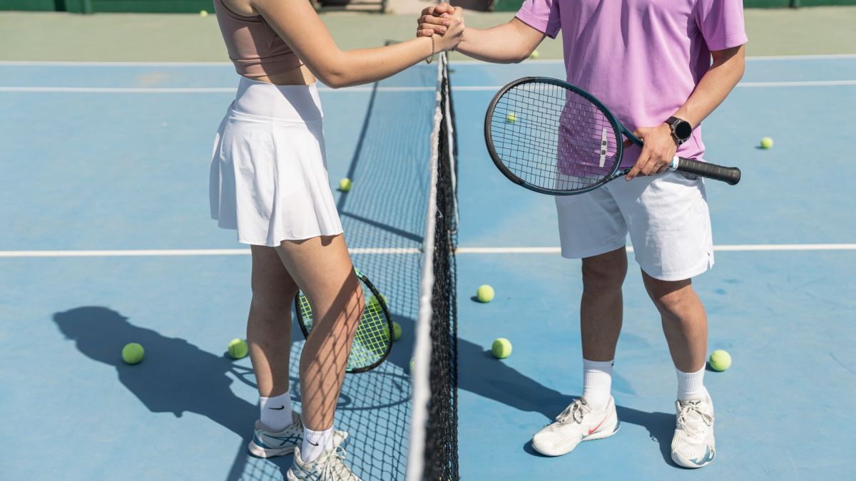 Two tennis players shaking hands over the net on a sunny day, symbolizing sportsmanship.