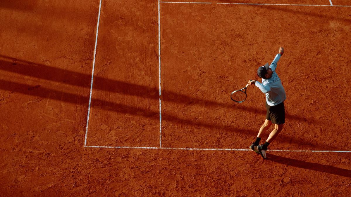 A dynamic shot of a tennis player serving on a clay court during sunset.
