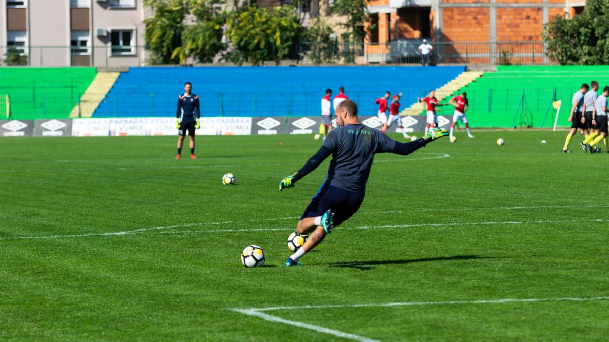 Soccer player in action during practice on a sunny day, kicking the ball on a green field.