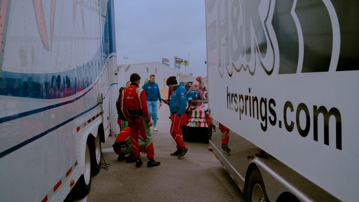 Race team in red uniforms preparing cars amidst trailers on race day.