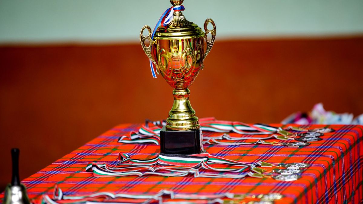 Golden trophy with ribbons and medals on a checkered table, symbolizing victory and achievement.
