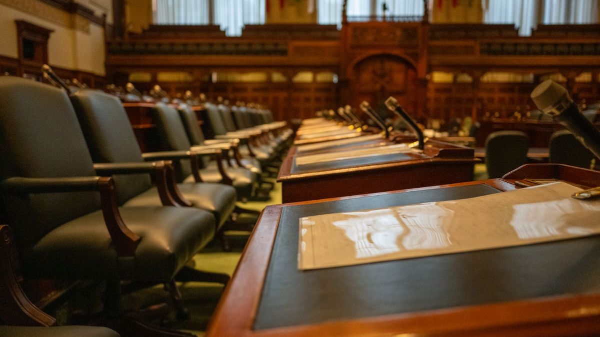 A detailed view of an empty legislative chamber with rows of desks and microphones, evoking governance.
