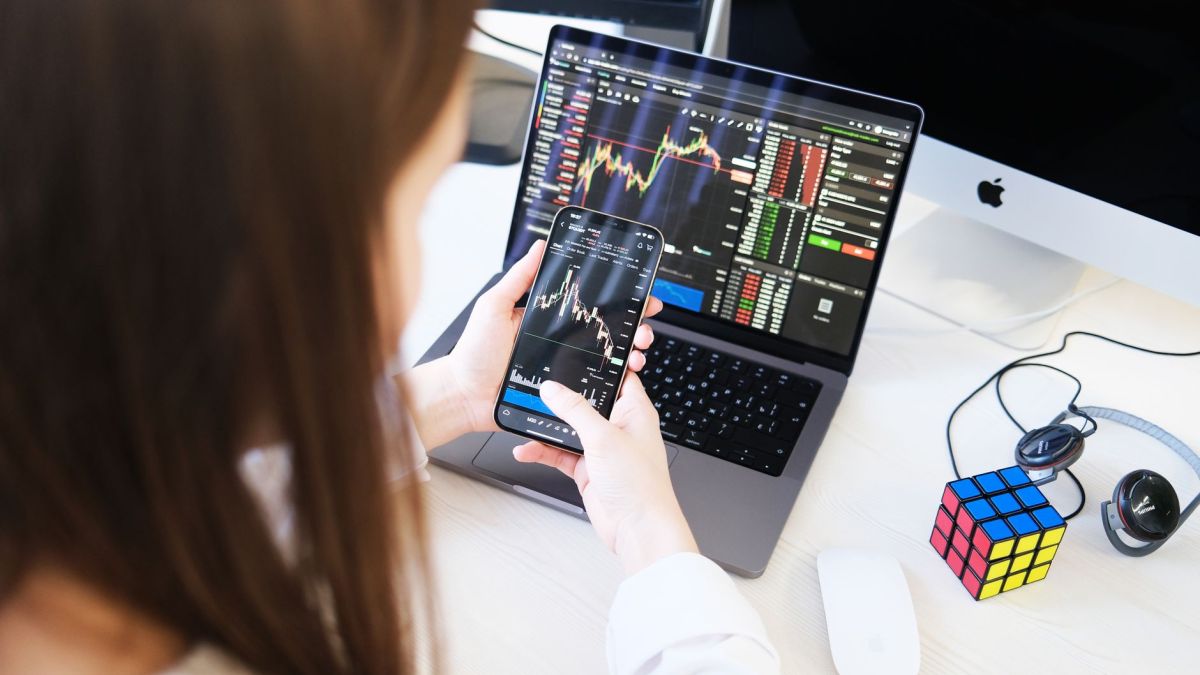 A woman trading cryptocurrency with charts on a smartphone and laptop, showcasing digital finance technology.