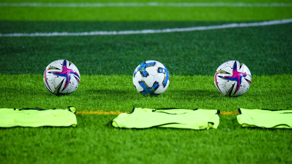 Three soccer balls and training bibs on a lush green field in Rawalpindi, Pakistan.