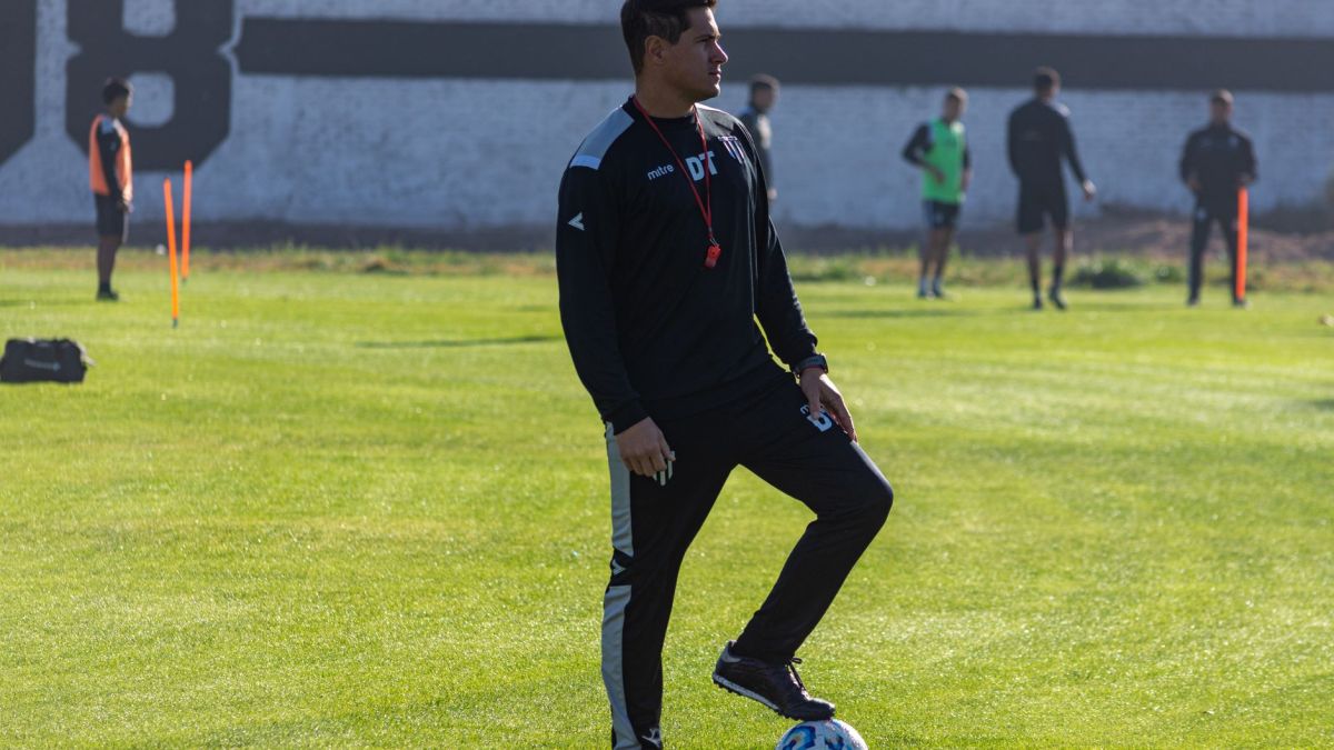 Adult soccer coach guiding players during outdoor training on a sunny day.