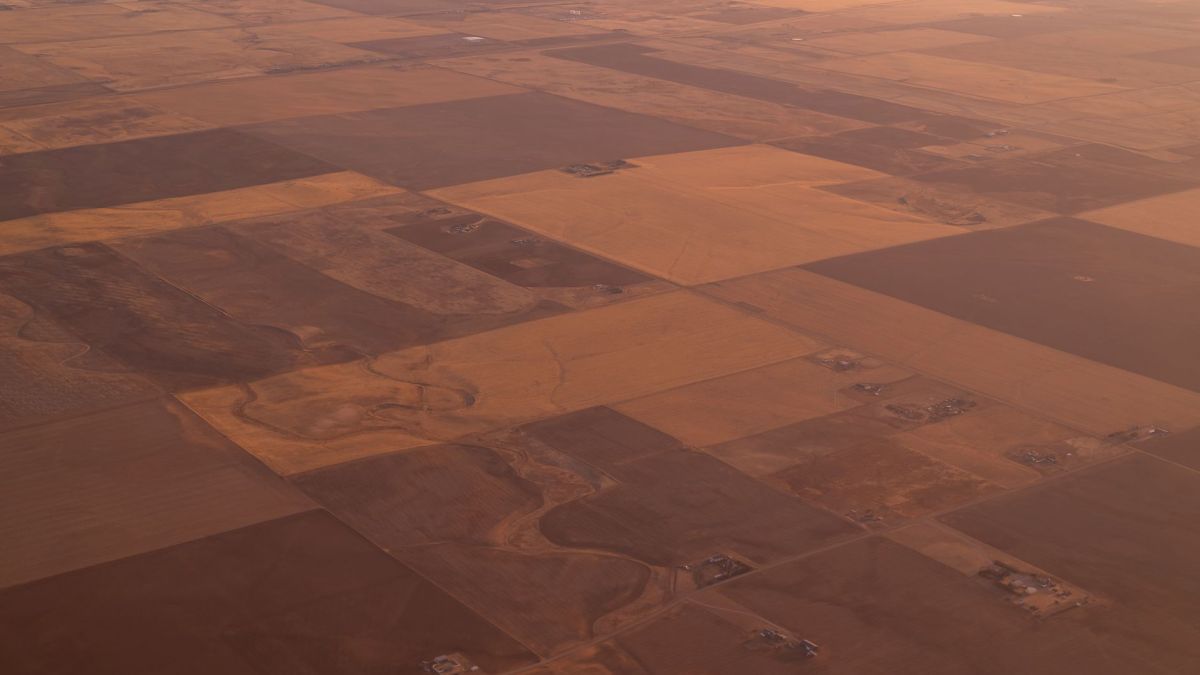 Aerial shot capturing the vast farmland landscape at twilight with rich browns and yellows.